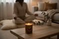 Load image into Gallery viewer, Lit wood-grain ceramic candle on a low wooden table, with a person seated on a cushion in the background.